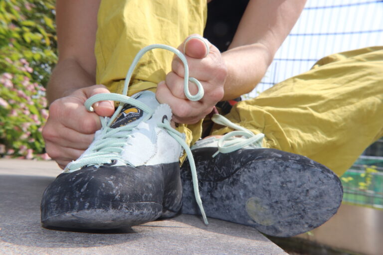 Nahaufnahme von zwei Händen, die einen Kletterschuh binden