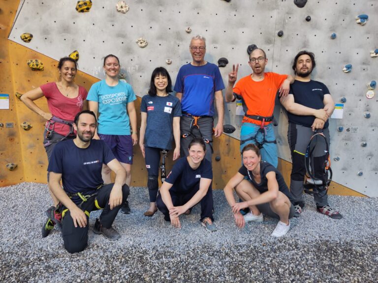 Gruppenbild vor eienr Kletterwand. Sechs Personen stehen in einer Reihe drei weitere kniene vor ihnen.