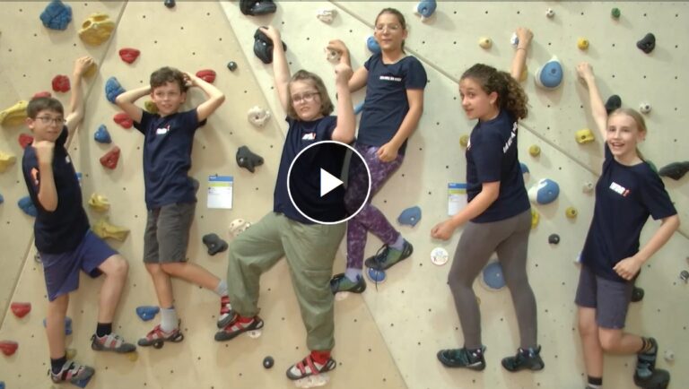 An einer Kletterwand hängen 6 Kinder in IWDR-T-Shirts und schauen in die Kamera.