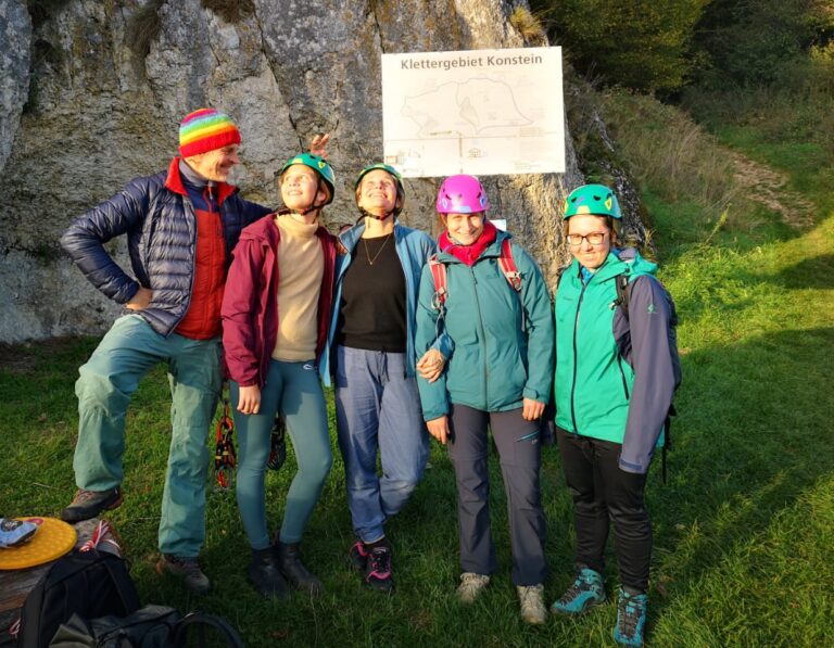 Eine Gruppe von 5 Personen, ein Mann und vier Frauen stehen in der Abendsonne vor einer Felslandschaft und einen großen Schild mit der Aufschrift: "Klettergebiet Konstein"